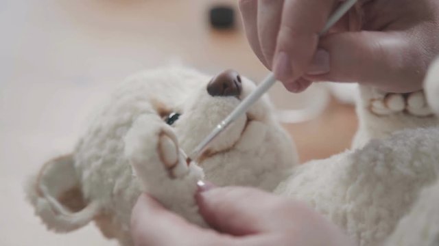 A thin brush in the hands of the artist to create soft toys - drawing details of a handmade toy. The master draws the dividers on the foot for a teddy bear in an old-fashioned style.