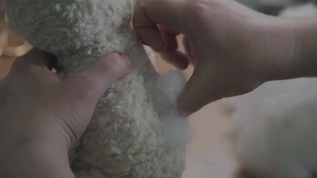 Repair of plush toys: female hands sew a teddy bear. Creating soft handmade toys. Broken toy vintage bear cub - restoration of an old toy. Sew a soft toy: the seam on the back.