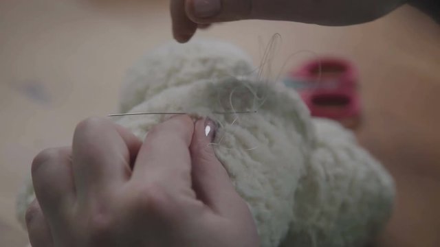 Repair of plush toys: female hands sew a teddy bear. Creating soft handmade toys. Needle and thread in hand of a woman - she sews the details of a soft toy. The process of sewing the details of a toy