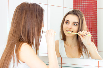 beautiful young girl brushing her teeth in front of the mirror