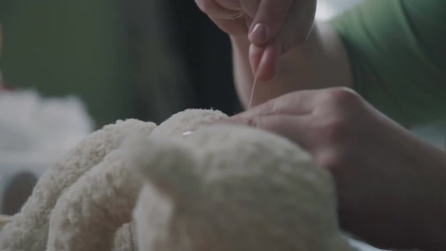 Repair of plush toys: female hands sew a teddy bear. Creating soft handmade toys. Broken toy vintage bear cub - restoration of an old toy. The process of sewing the details of a toy.