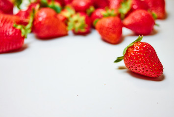 Berries of strawberries of different shapes and sizes are scattered randomly on a white background.