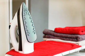 Iron for ironing on the ironing board with a pile of towels near