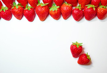 Equal row of strawberries on top of photo and 2 strawberries in bottom corner on white background
