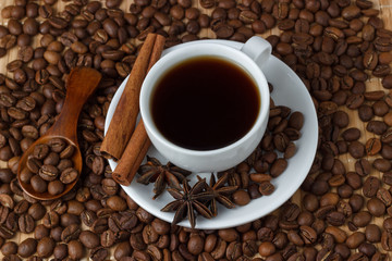 Coffee in a cup with cinnamon sticks on the background of coffee beans