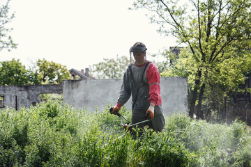 worker mowing green grass with trimmer.