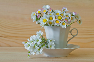 Obraz na płótnie Canvas Bouquet of white of field flowers in a cup with a plate on a wooden background