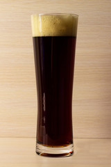 Tall glass of dark beer over a dark background lit yellow