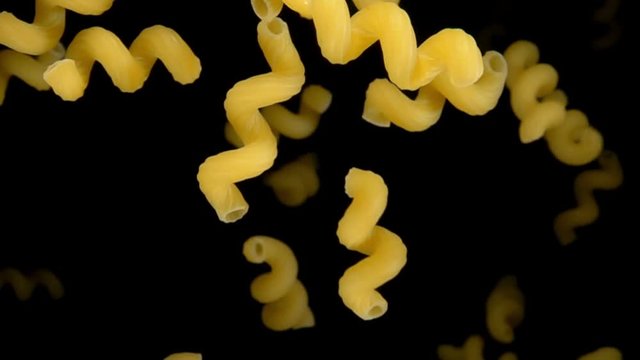 Pasta cellentani bouncing against to the camera on a black background in slow motion