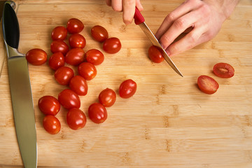 Man's hands cutting fresh tomatos in the kitchen, preparing a meal for lunch. Topdown view.