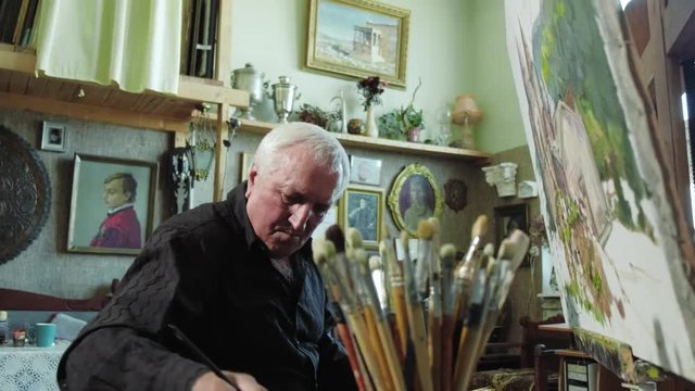 An elderly artist writes a picture in his studio 4k