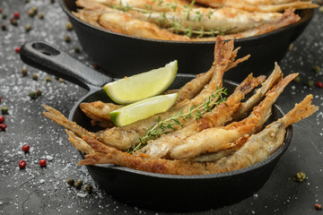 Fried smelt in a frying pan on the table with spices, lime and thyme. Small crispy fish. Selective...