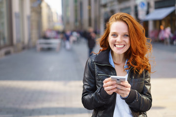 lachende frau steht in der einkaufsstraße und hält ihr handy in der hand