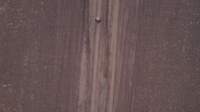 Aerial view of female farmer walking on dirt country road between two arable cultivated fields