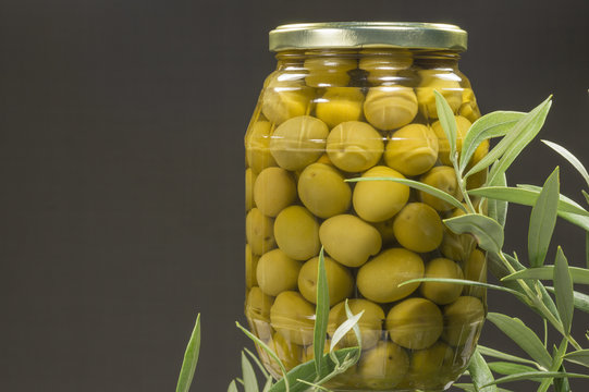 Un recipiente de cristal con aceitunas en conserva, hojas de olivo junto al recipiente
