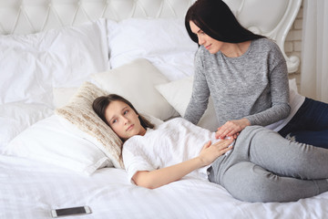Supportive mother helping her worried teenage daughter lying on the bed