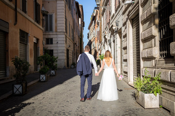 Obraz premium Young beautiful bride and groom on the wedding walk through the streets of old Rome, Italy.