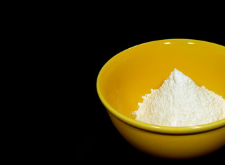 White dry flour in yellow ceramic bowl on black background with free space for text and design 