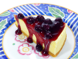 Piece of baked cheesecake with blueberry sauce served on vibrant colored pattern plate 