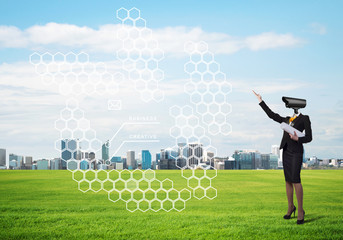 Camera headed woman standing on green grass against modern cityscape