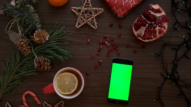 Top view man hand using smart phone with green screen. Finger scrolling pages down on touchscreen. Christmas details on wooden table background. Chroma key