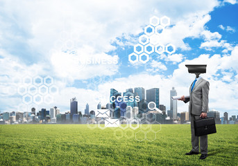 Camera headed man standing on green grass against modern cityscape