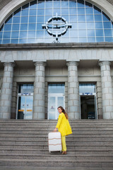Young woman dressed in yellow suit with suitcase rising up the stairs of railway station and looking back