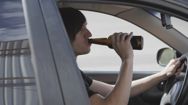 Guy drinks beer while driving a car. Drunk driver