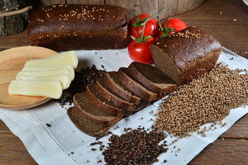 Sliced bread and cheese with tomatoes on textile and wood on background