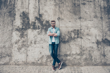 Full length portrait of young red bearded man in stylish casual outfit and glasses standing outside and looking harsh