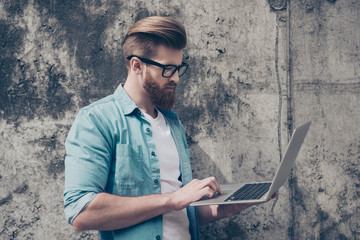 Young handsome bearded entrepreneur is working outdoors on his laptop. Very stylish and trendy