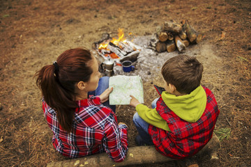 Camping in the forest. Mom and son are sitting near the fire preparing coffee and looking at the map.