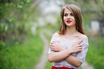 Portrait of beautiful girl with red lips at spring blossom garden, wear on red dress and white blouse.