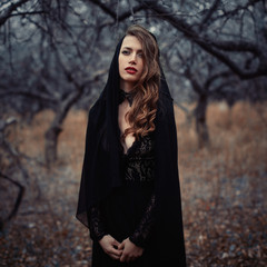 Beautiful girl in in black vintage dress with curly hair posing in the woods. Woman in retro dress lost in the forest. Worried sensual emotion . Retro fashion