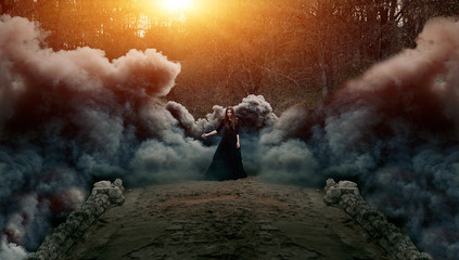 Young attractive Witch walking on the bridge in heavy black smoke. - obrazy, fototapety, plakaty