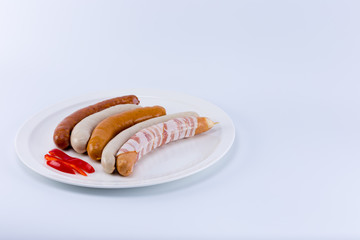 Five different raw german sausage wurst with sliced red bell pepper on a white dish isolated on white background