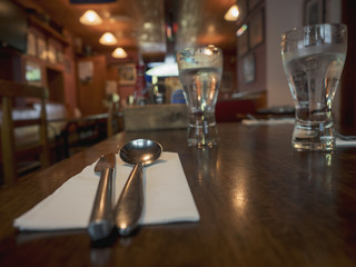 Knife, spoon, cold drinks  on a table  in focus traditional Irish pub interior out of focus.