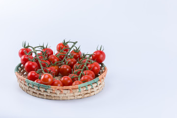 Juicy ripe cherry tomatoes on a straw basket isolated on white background