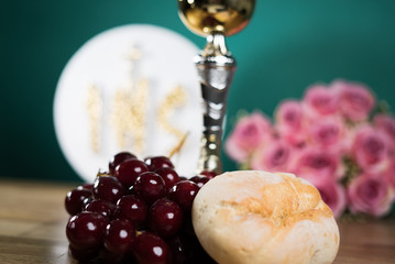Holy Communion, chalice, flowers and grapes on wooden table