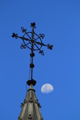 Cruz de hierro forjado sobre cielo azul con luna blanca.