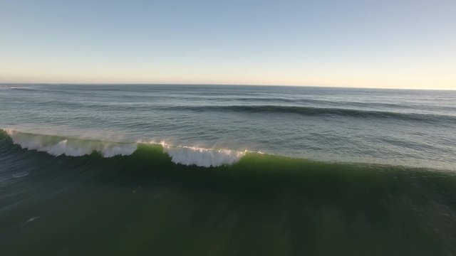 Aerial view of green surfing waves breaking on rocky coastline