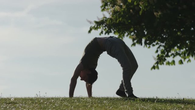 Male contortionist walks along grass in a crab pose