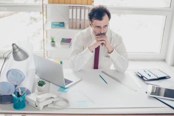 Thoughtful businessman in formal clothes sitting at the table at his office and thinking how to increase profit from new business project