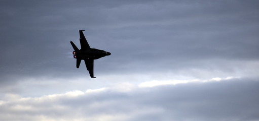 Silhouette of F18 Hornet fighter aircraft in flight. Clouds in the background.