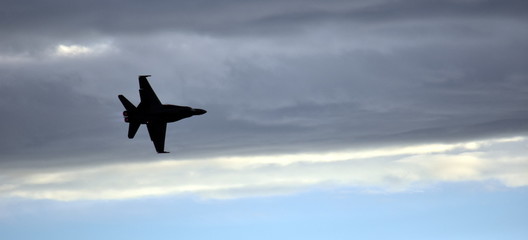 Silhouette of F18 Hornet fighter aircraft in flight. Clouds in the background.