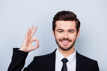 Confident young smiling smart-clothed freelancer showing ok-sign on gray background