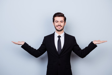 Portrait of handsome young smiling man in suit asking to make a choice between two products on his palms