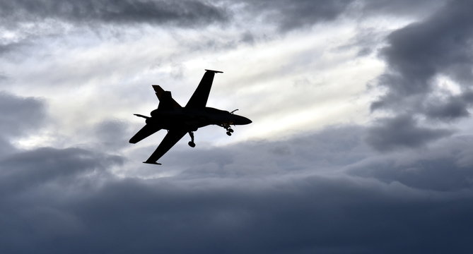 Silhouette of F18 Hornet fighter aircraft in flight. Clouds in the background.