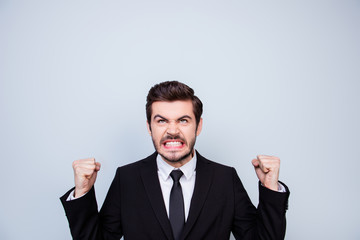 Young very angry man in black suit showing fists and looking up on copyspace over his head in rage