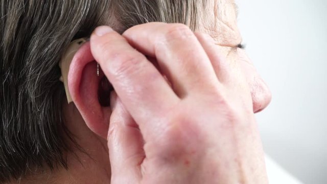 Closeup senior woman with hearing aid in her ear. Health care, hear amplify, device for the deaf. 4K ProRes HQ codec